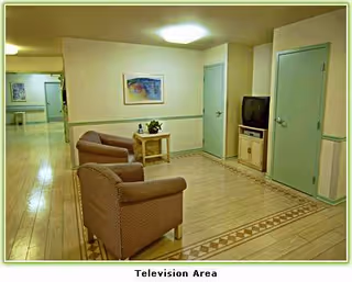 Muted-hued lounge area with two chairs, a small table, and a TV by a hallway.