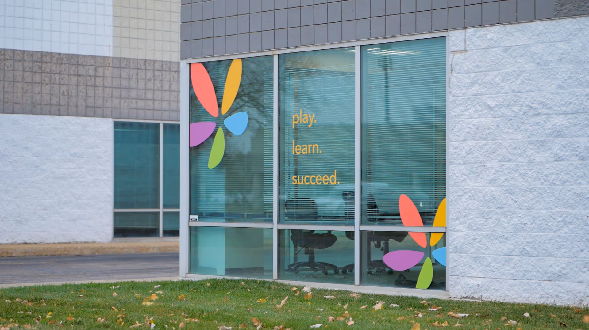 Exterior building facade with glass windows displaying colorful decals and the words play. learn. succeed.