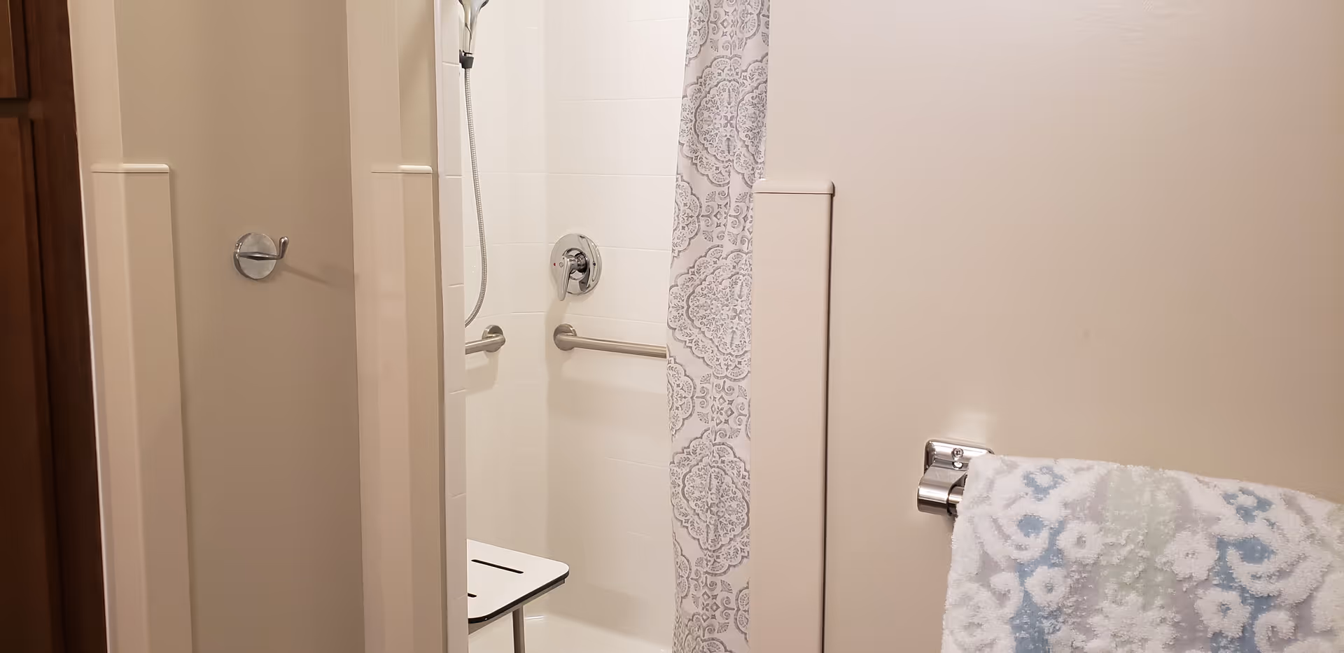 Accessible bathroom in a senior living facility with shower, grab bars, and patterned curtain.