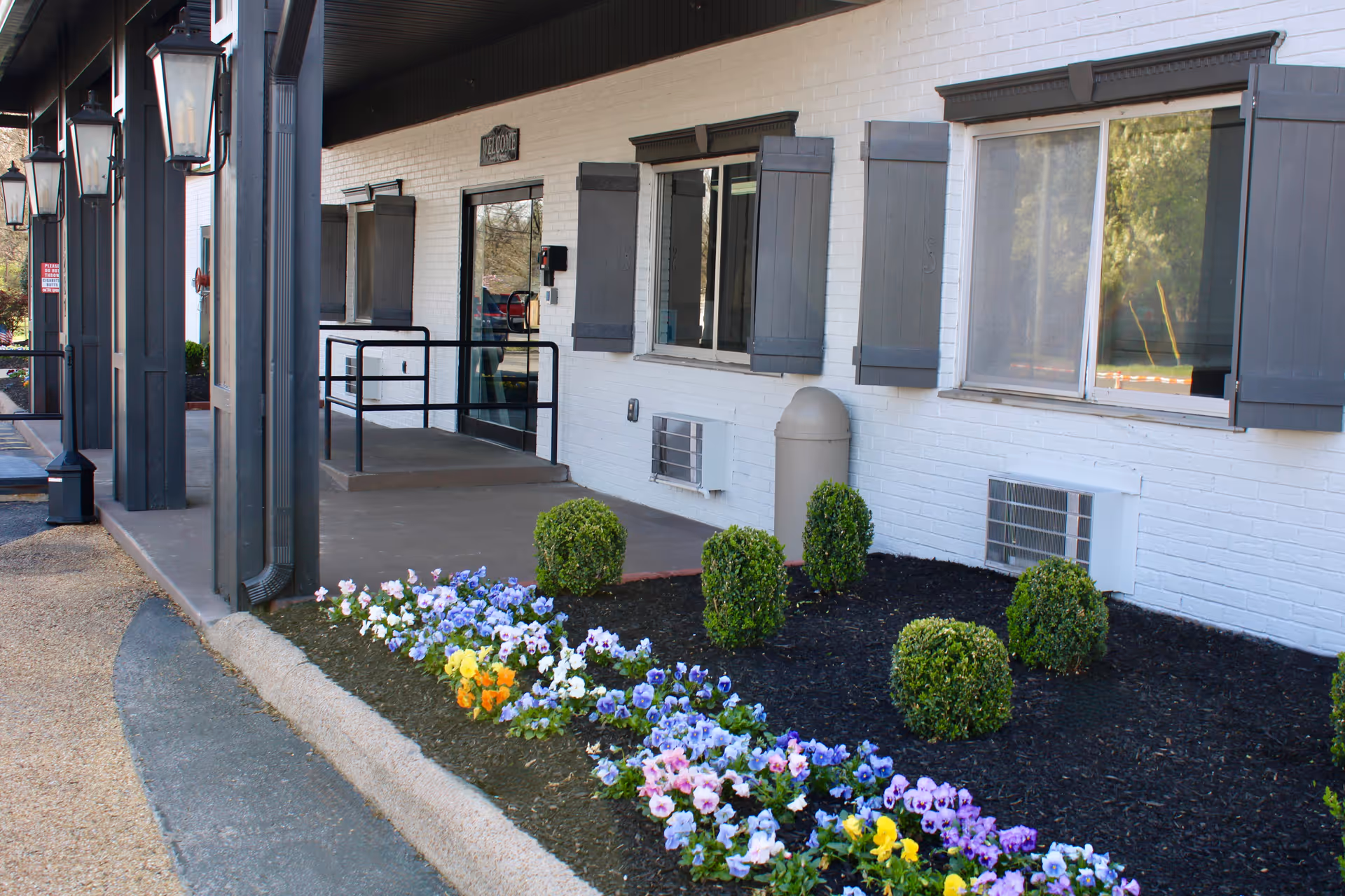 Exterior entrance of Franklin Wellness and Rehabilitation Center with flowers and trimmed shrubs.