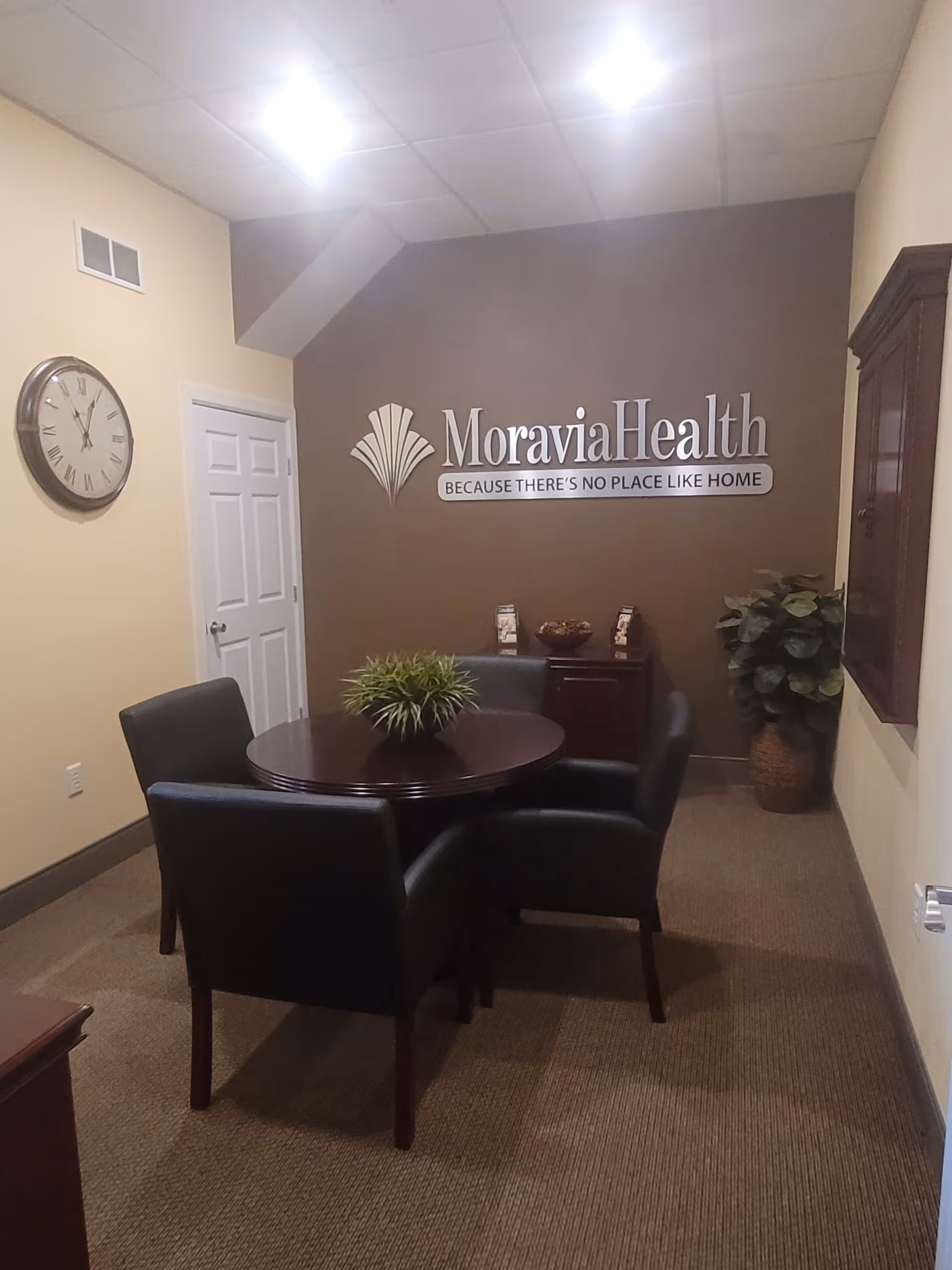 Lobby-style interior with MoraviaHealth logo, round table, four chairs, and plants.
