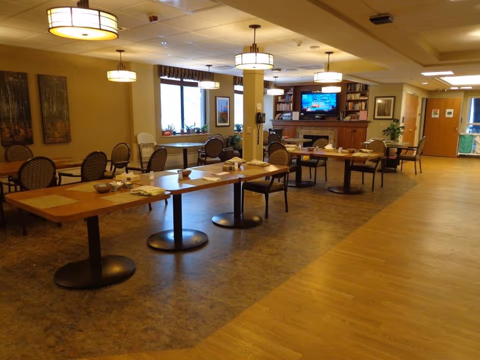 Senior living dining area with multiple tables, chairs, and a television in the background.