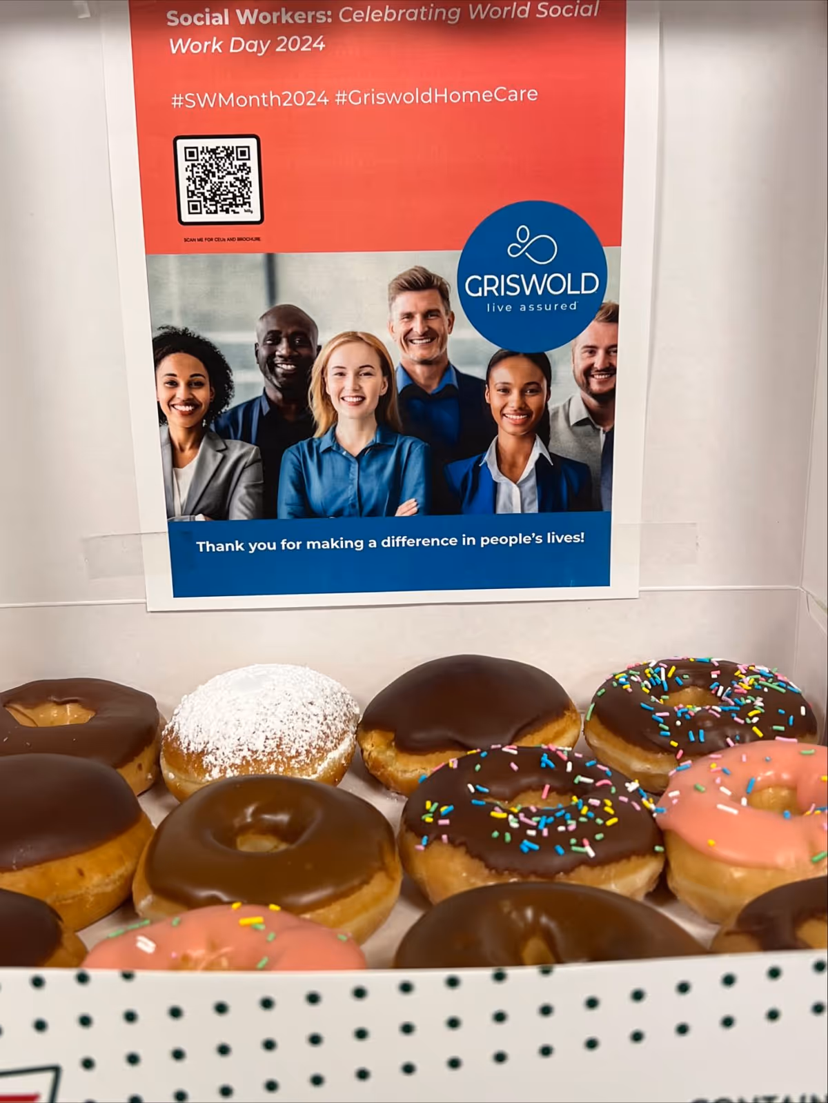 Donuts in a display box beneath a Griswold Home Care poster.