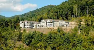 Hillside senior living facility with white buildings sits among dense trees and forested hills.