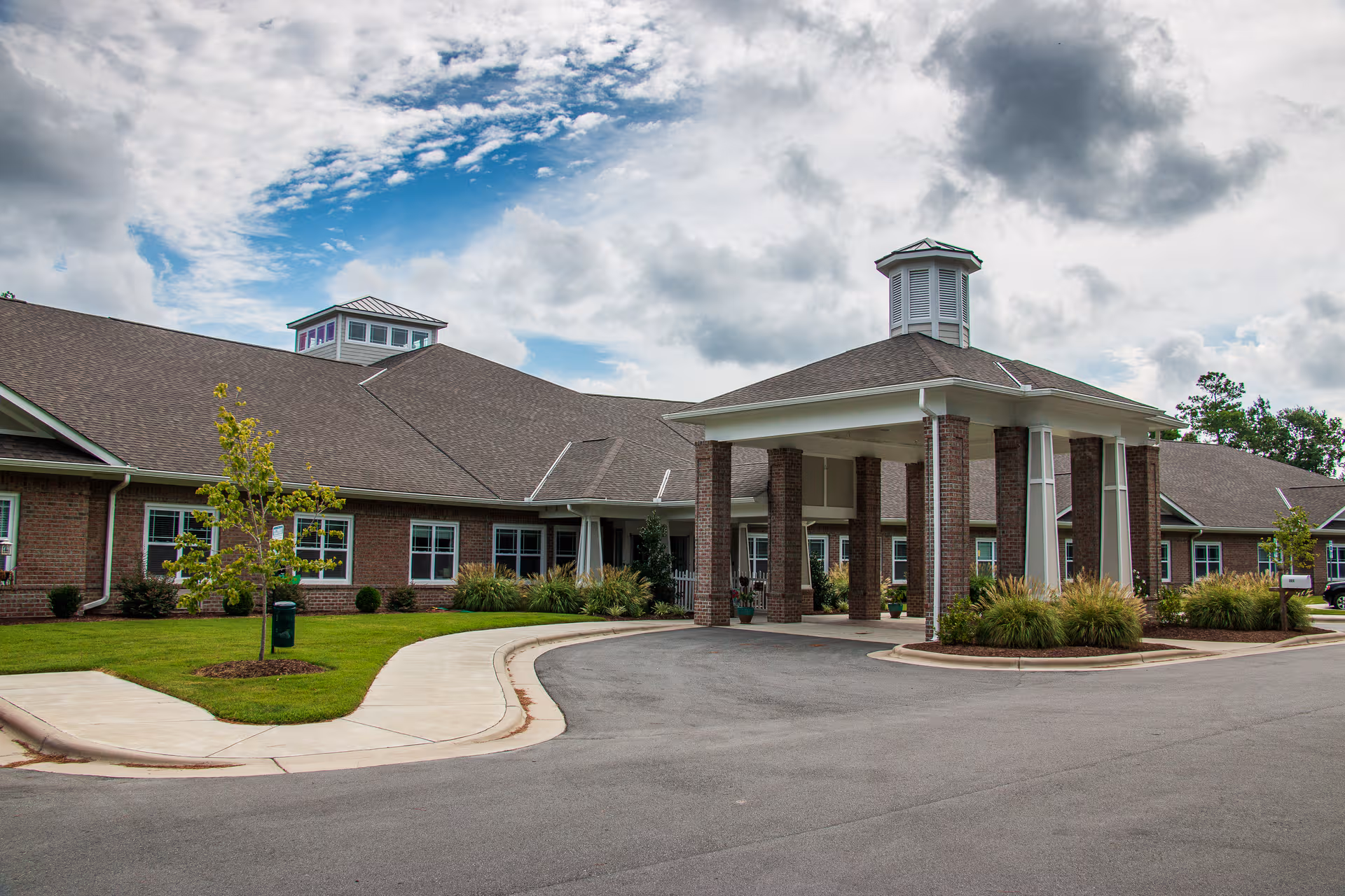 Brick senior living facility with a covered entrance, circular driveway, and manicured landscaping.