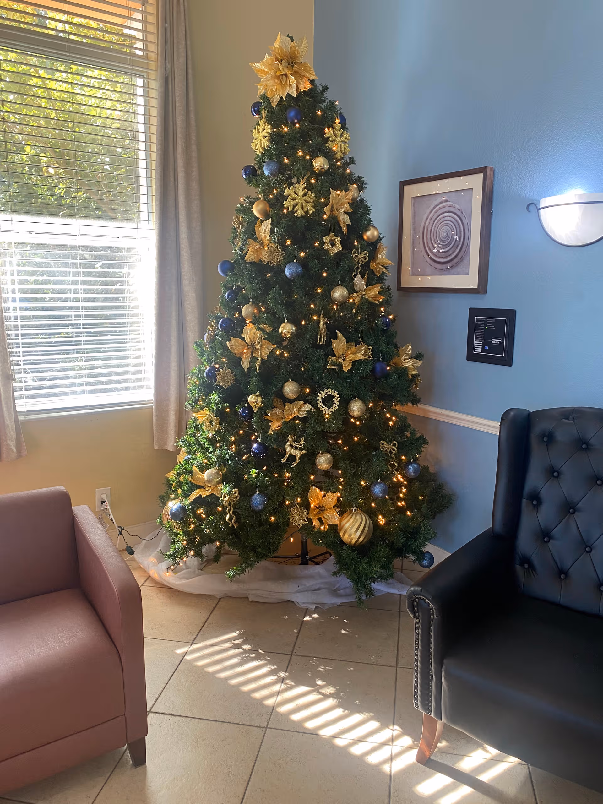 Decorated Christmas tree with gold and blue ornaments in a bright Harmony House of Ocala lobby.