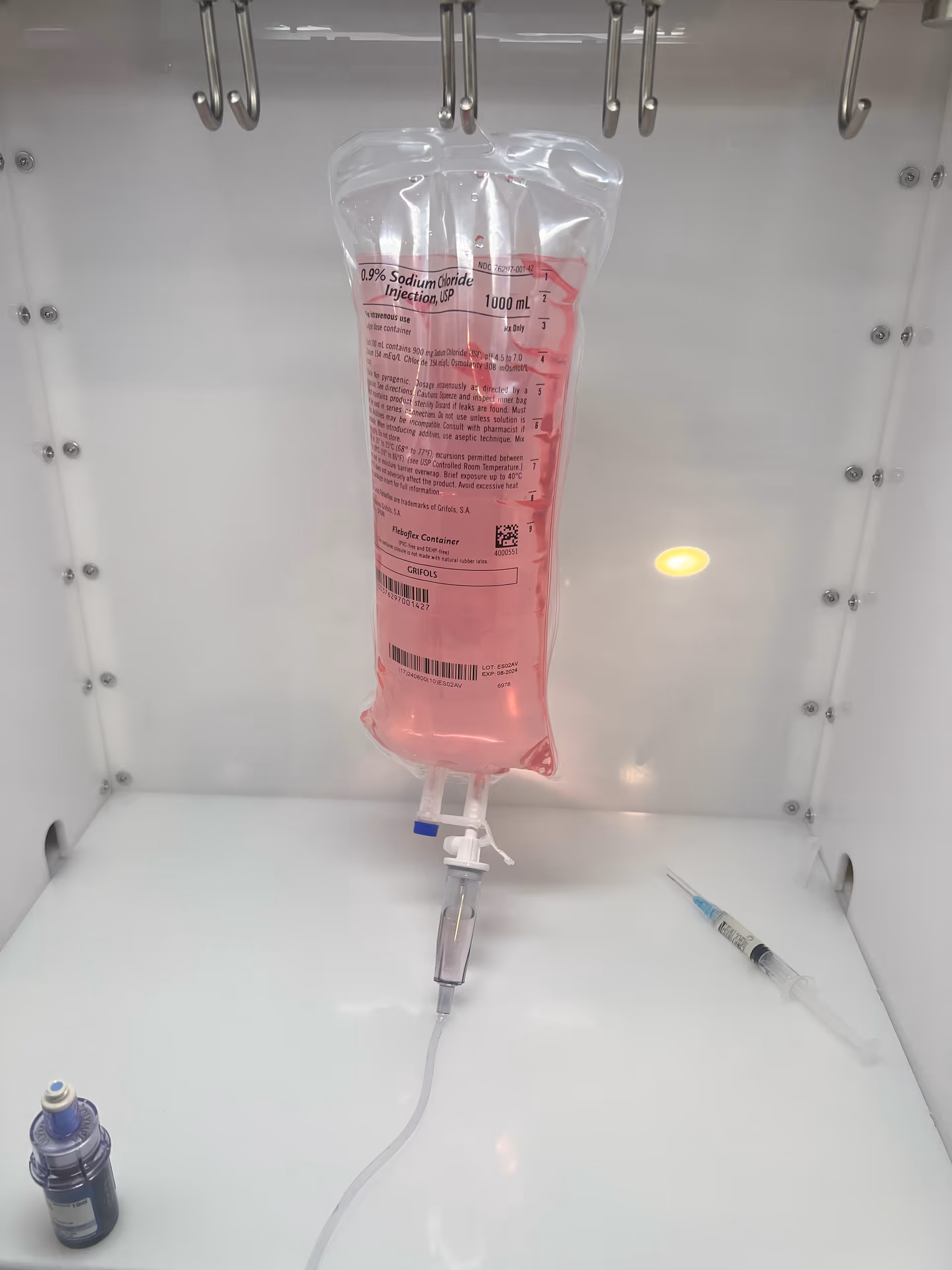 Pink IV fluid bag suspended in a cabinet with syringe nearby