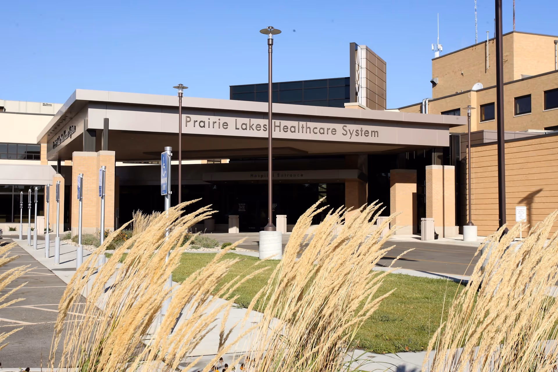 Front exterior of Prairie Lakes Healthcare System with entrance, pathway, and ornamental grasses.