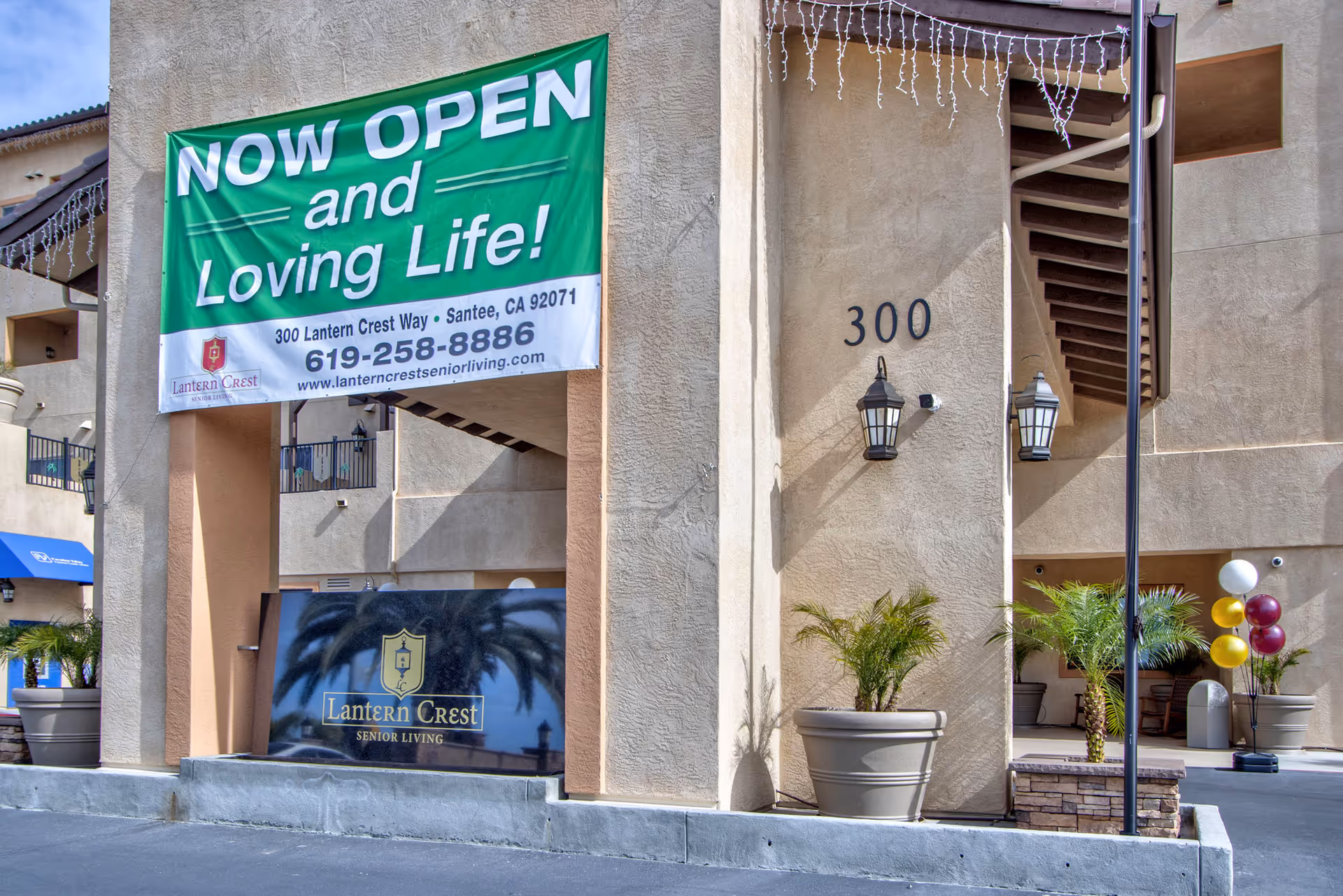 Exterior of Lantern Crest Senior Living with a large green Now Open banner.