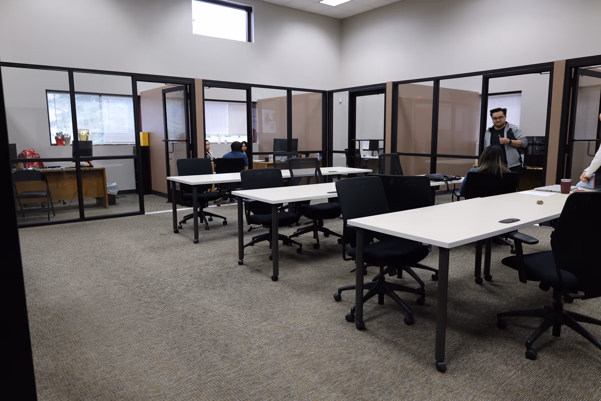 A conference room with glass partitions, white tables, and office chairs.