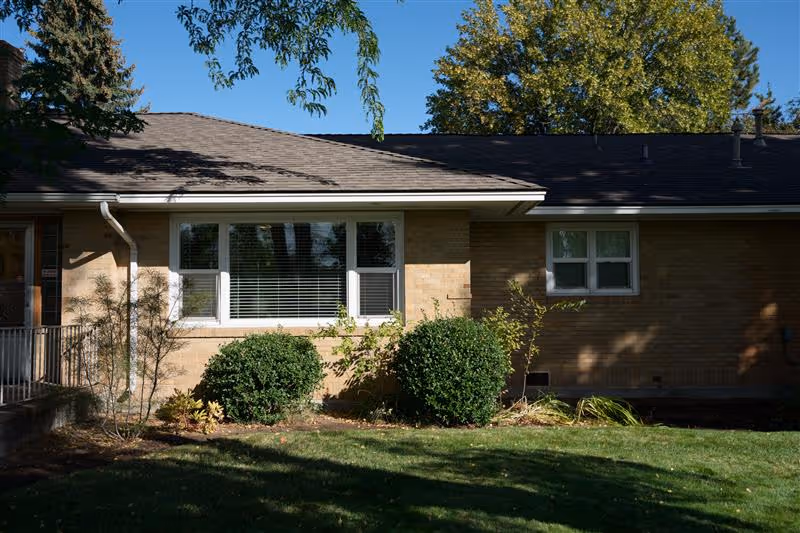 A brick senior living facility exterior with windows, shrubs, and a manicured lawn.