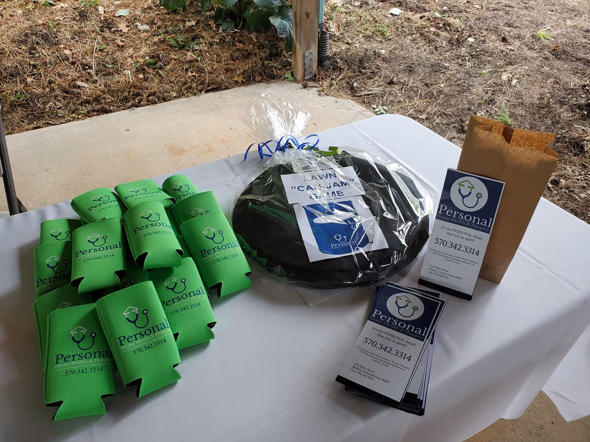 Outdoor table with green Personal HHC-branded items, brochures, and a gift bag.