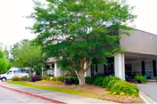 Exterior of a senior living facility with a covered entrance, landscaping, and a parked car.