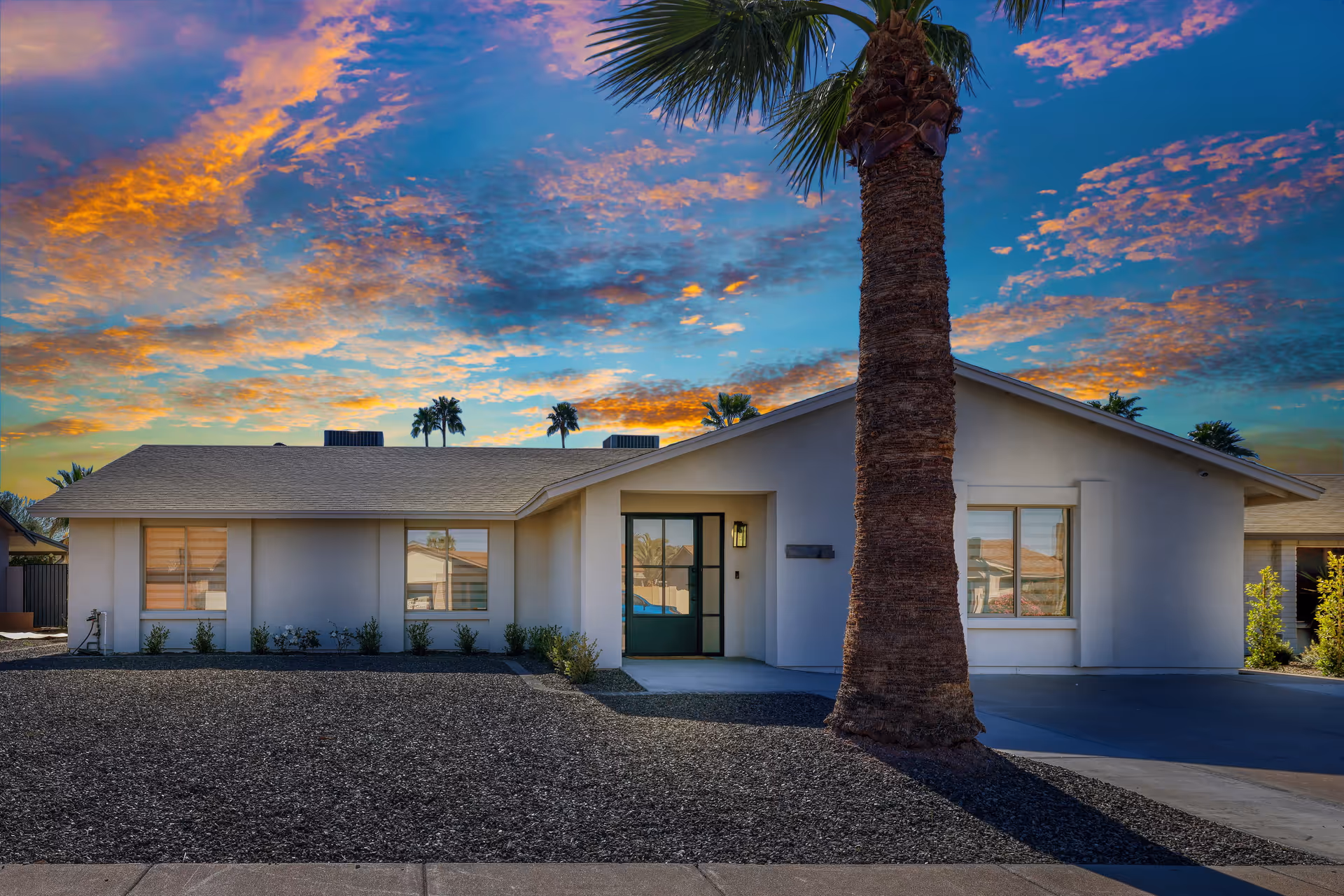 Front exterior of a single-story assisted living building with a palm tree at sunset.