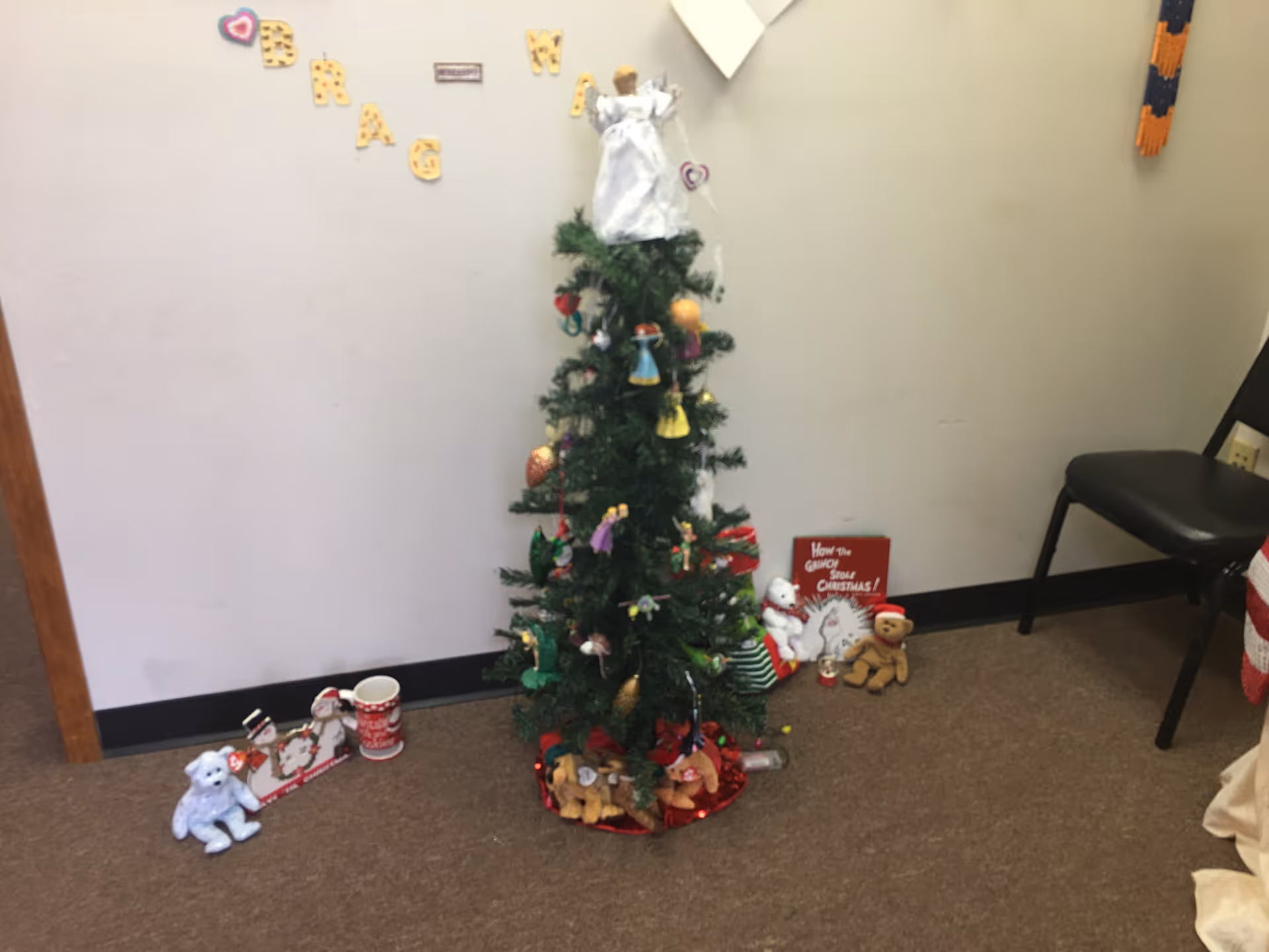 A Christmas tree with decorations and small gifts sits in a sparsely furnished interior corner.