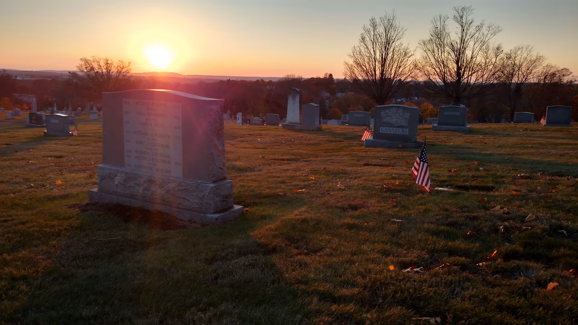 Sunset over a cemetery with headstones and American flags on the lawn.