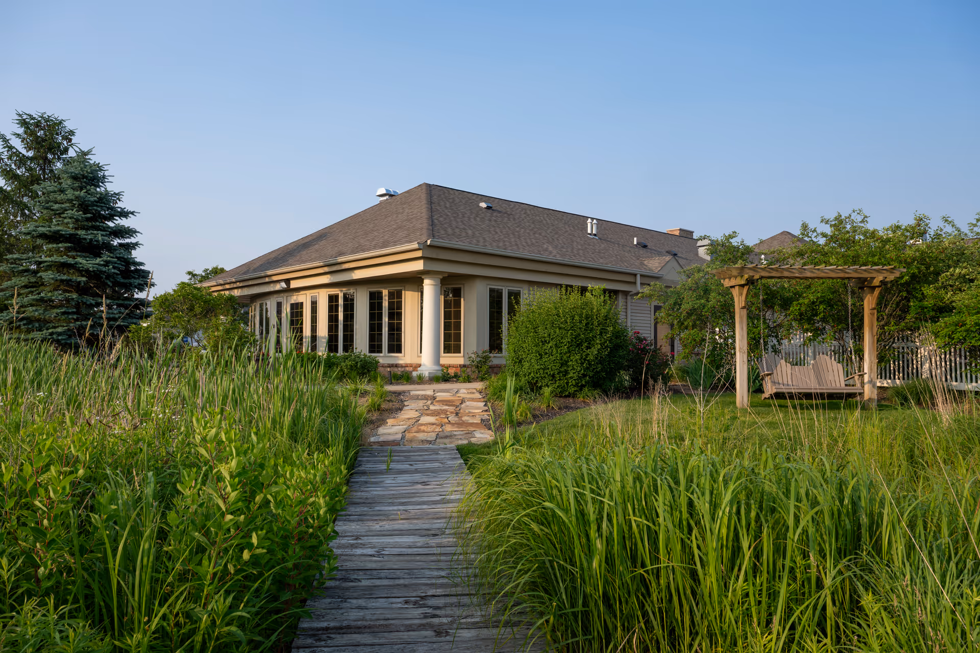 Single-story facility with stone walkway, lush landscaping, and a wooden pergola in the front yard.