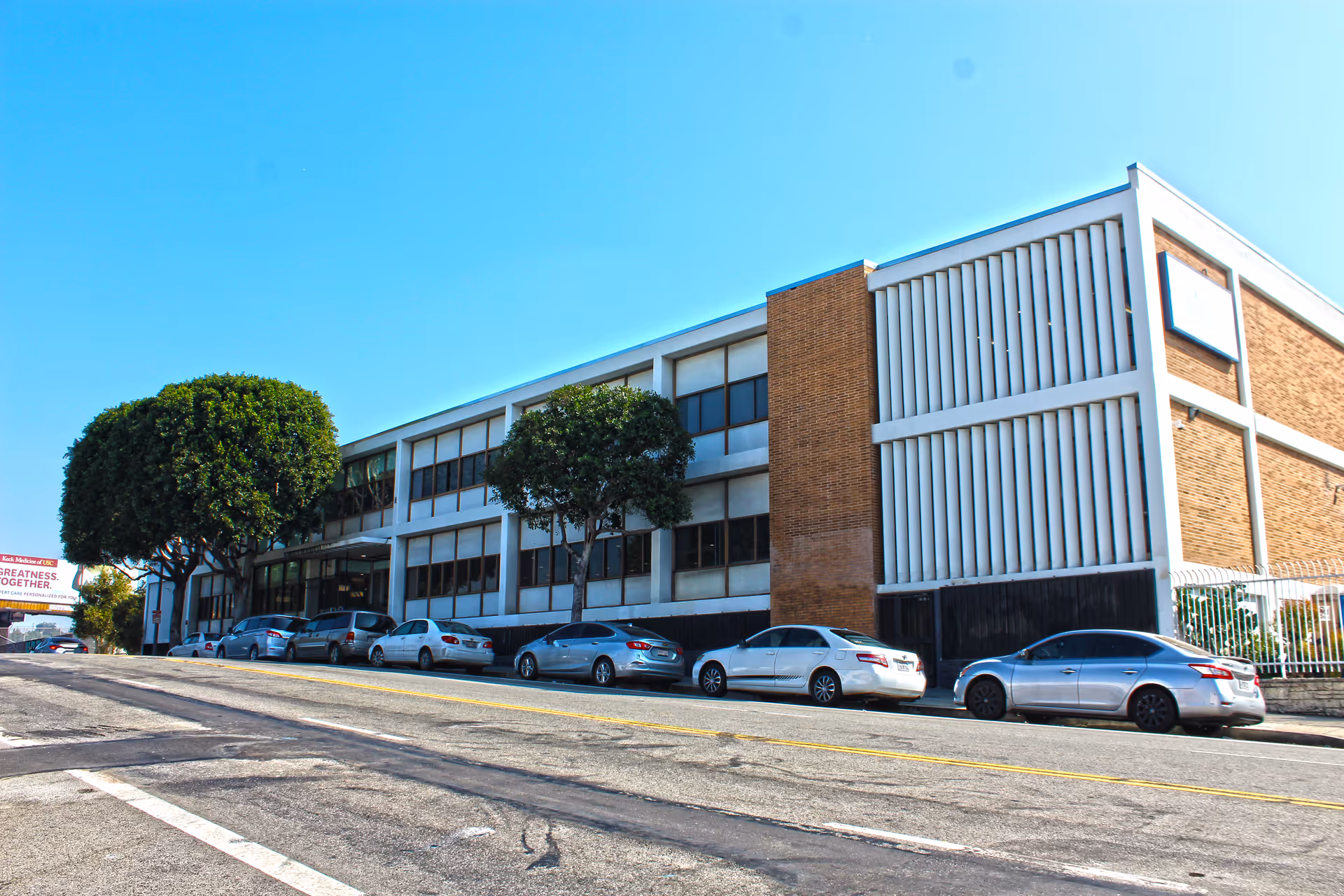 Exterior view of a multi-story senior living building with parked cars along the street.