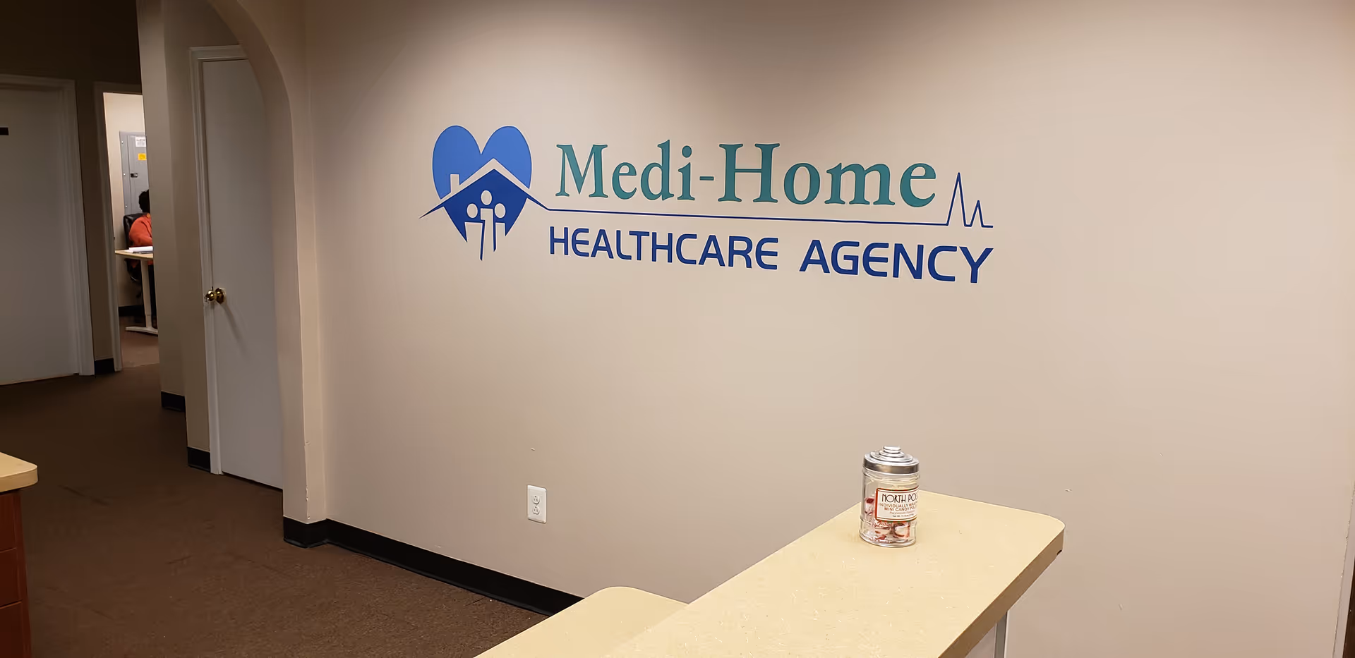 Interior hallway with Medi-Home Healthcare Agency logo on wall and counter in foreground.