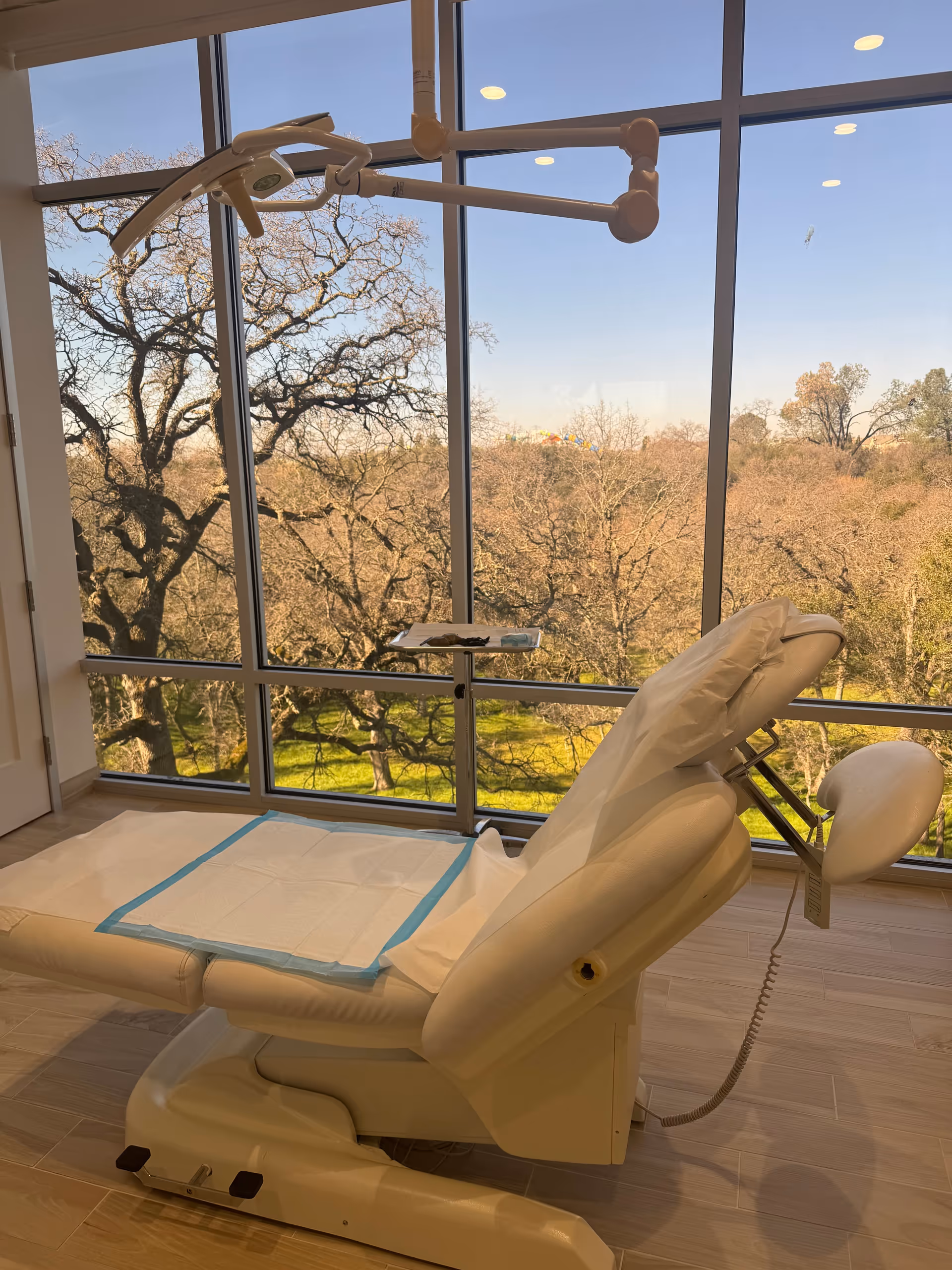 A white treatment chair in a bright clinic room with large windows