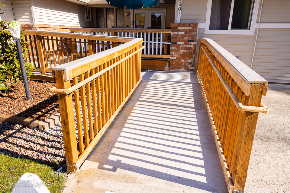 Wooden ramp with railings leads to the beige residential building entrance.