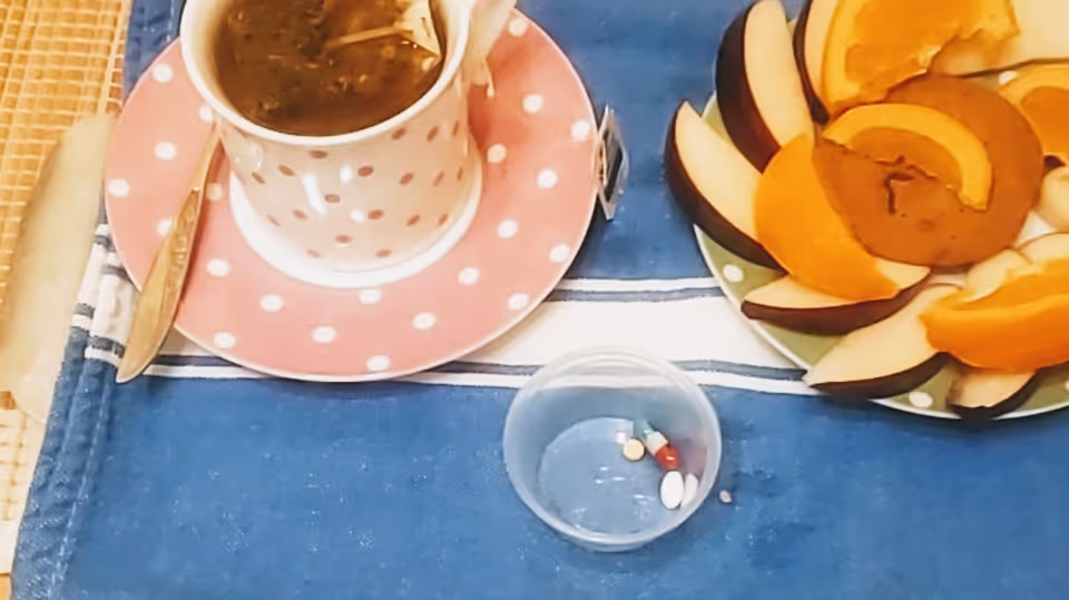 Coffee cup on pink polka-dot saucer, fruit plate, and pills on blue table.