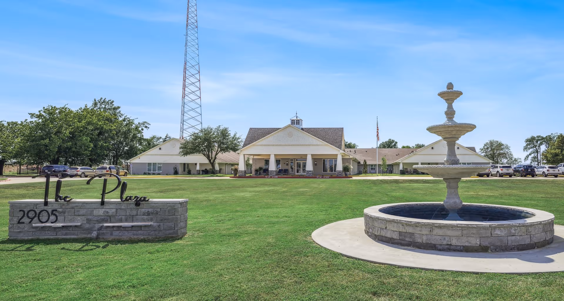 Front view of Lamar Place senior living facility with fountain, lawn, and cars.