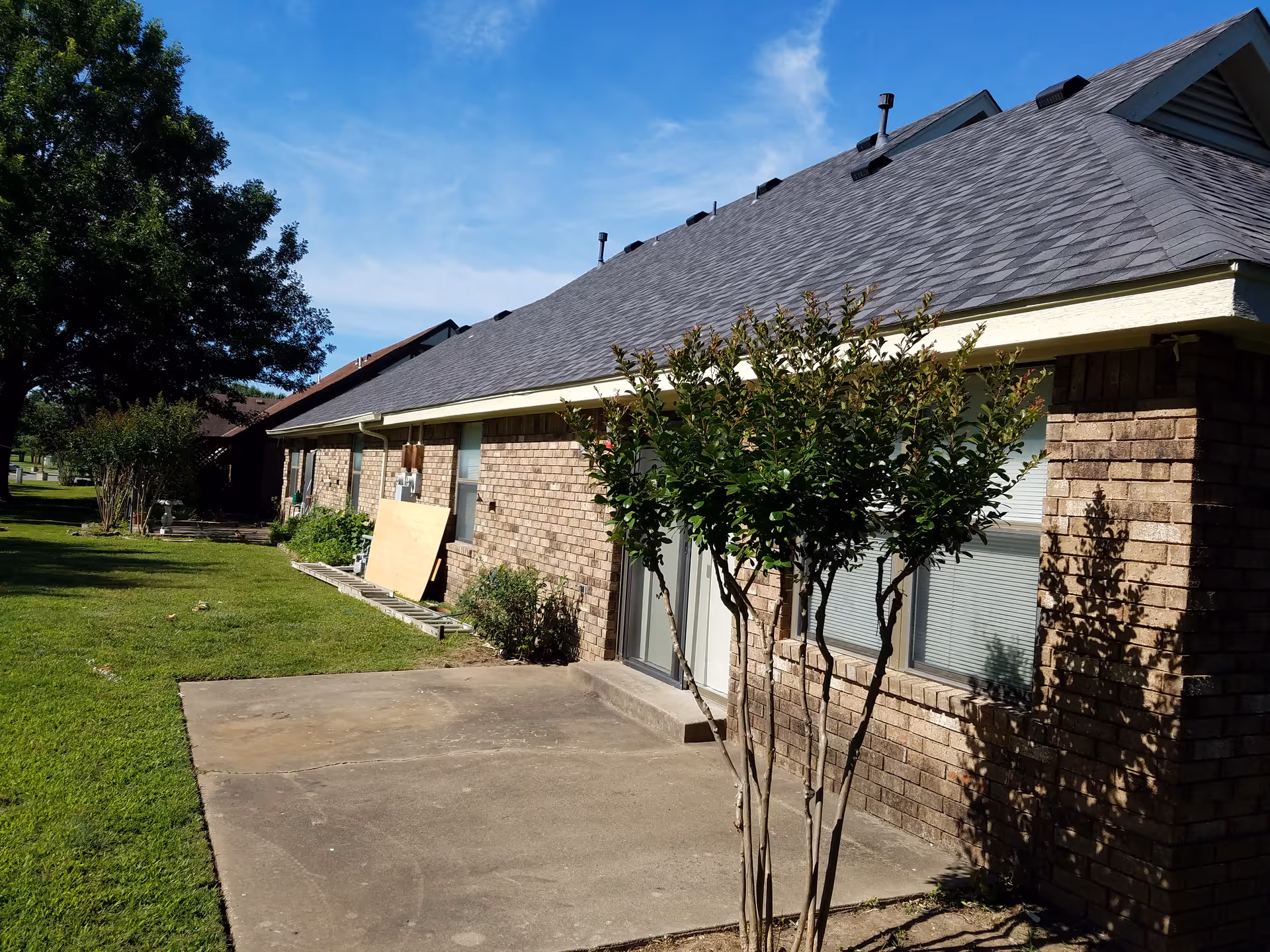 Single-story brick senior living facility exterior with a tree, lawn, and walkway.