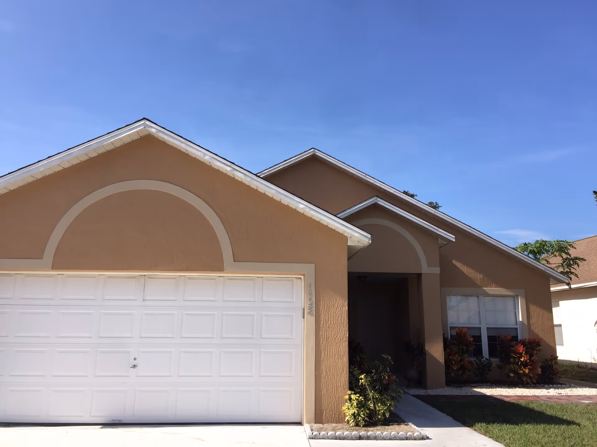 Front view of a tan single-story house with a white garage door.