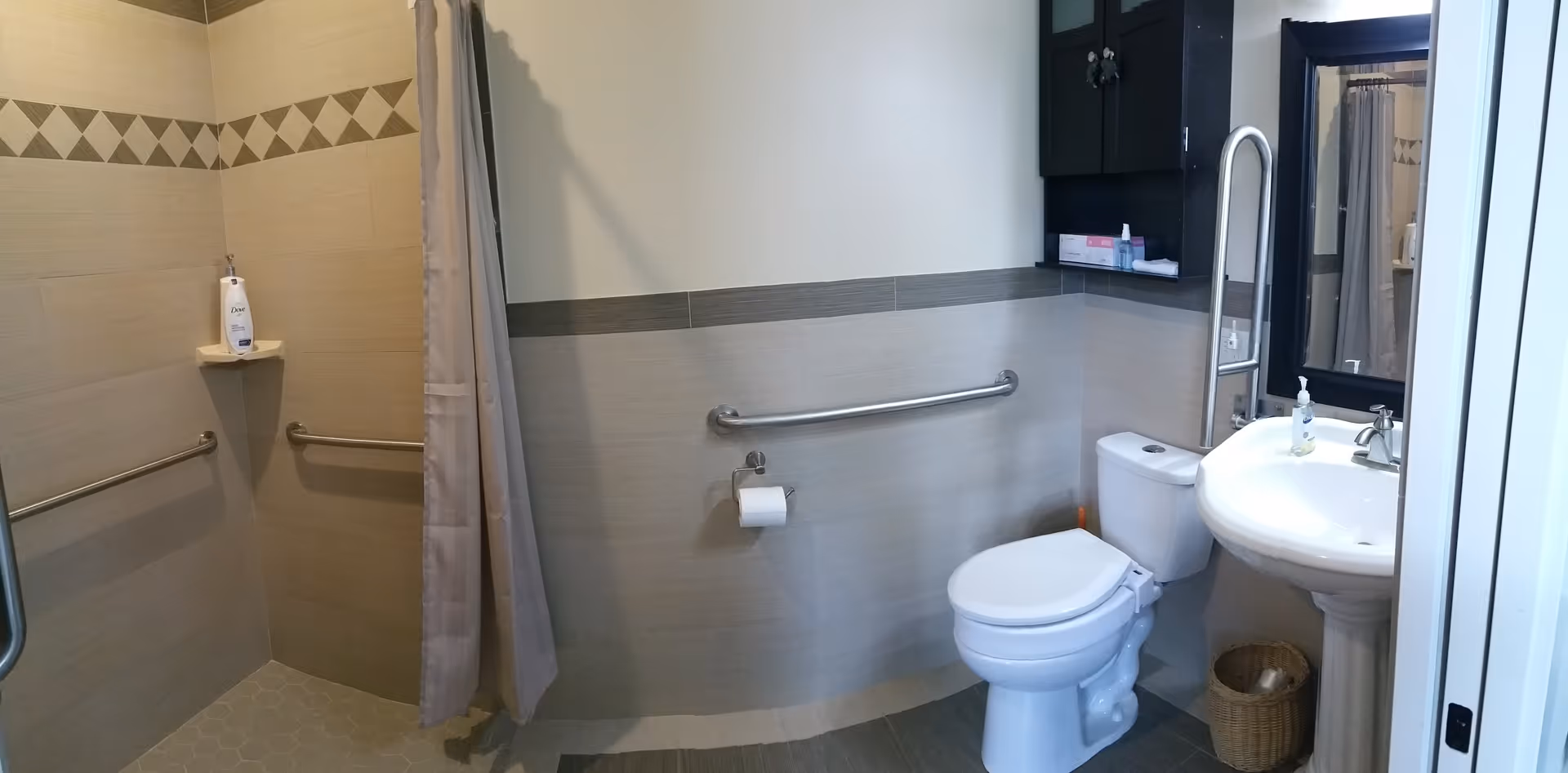 Accessible bathroom in a senior living facility with toilet, sink, shower, and grab bars.