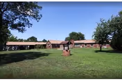 Front exterior of a long building with a green lawn and trees.
