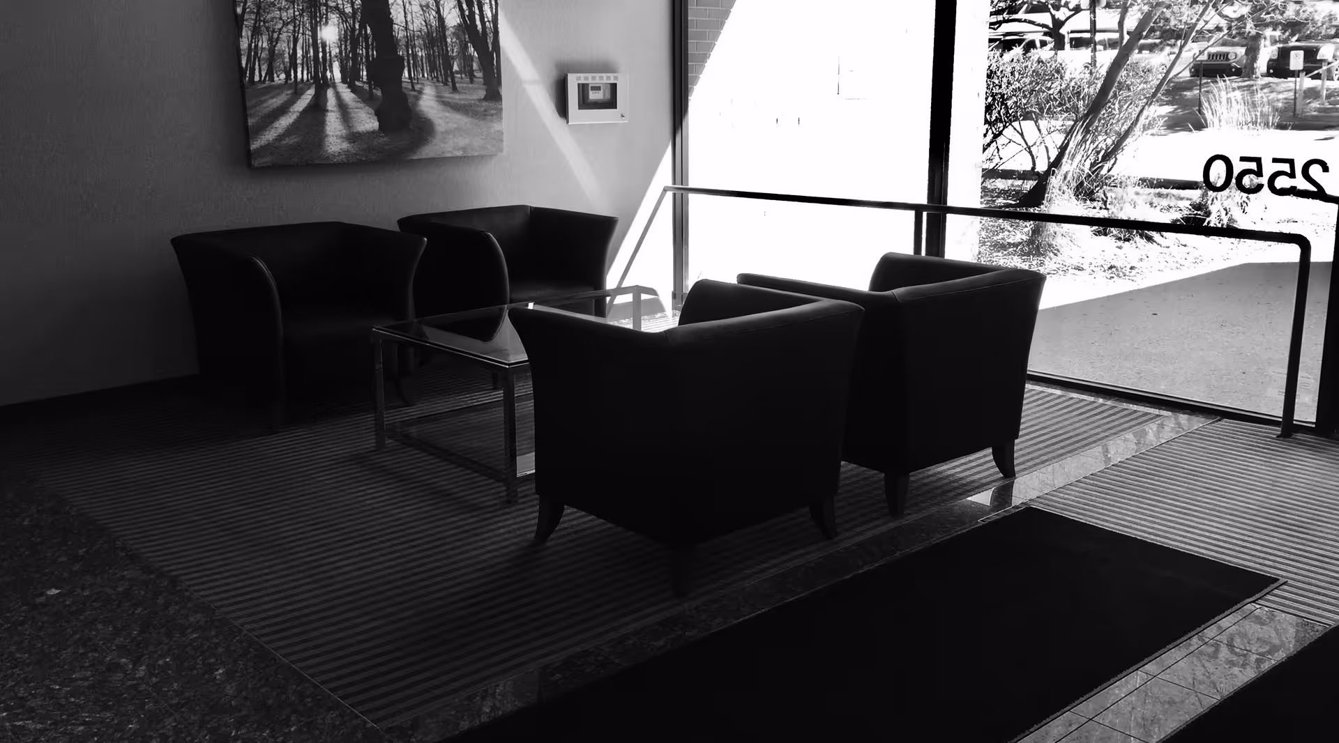 A modern indoor lounge with black chairs and a glass coffee table by a large window.