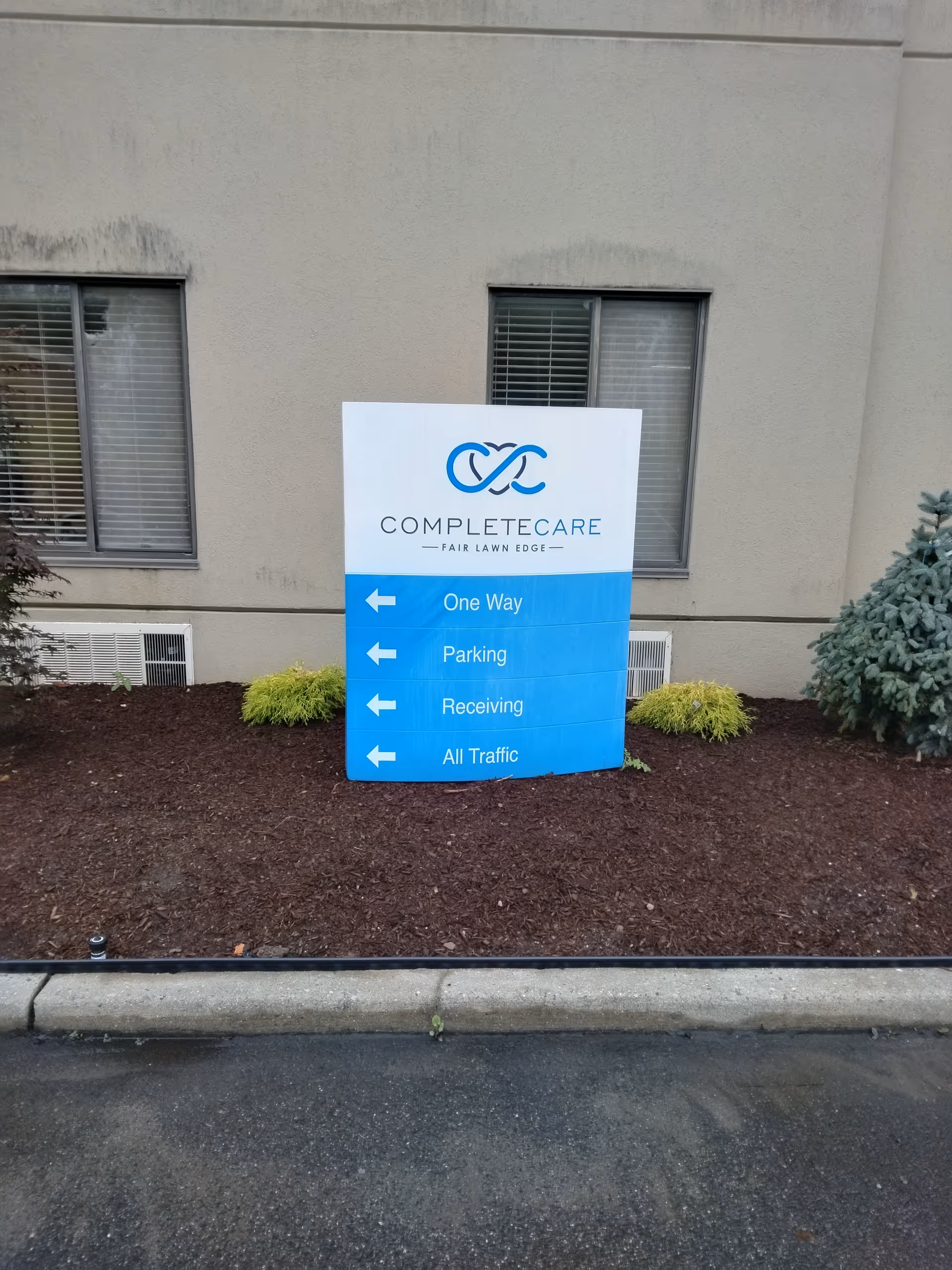 Exterior view of Complete Care building with blue directional sign in a mulched bed.