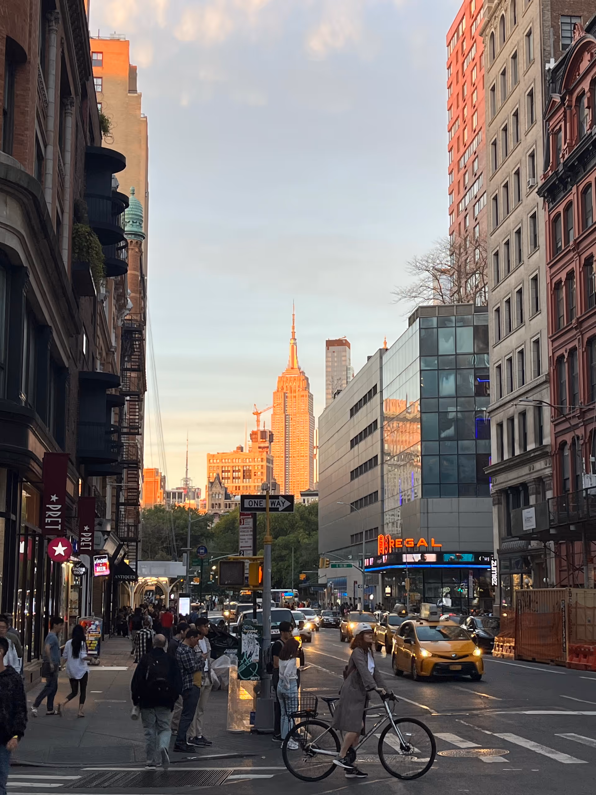 Busy urban street with pedestrians, a cyclist, taxis, and tall office buildings.