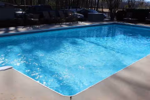 A bright outdoor swimming pool with lounge chairs and surrounding concrete deck.