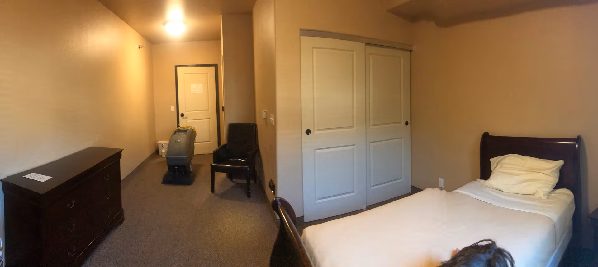 Bedroom with single bed, dresser, sliding closet, and chair in a senior living facility.