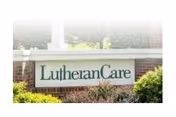 An exterior sign reading LutheranCare is mounted on a brick wall with greenery.