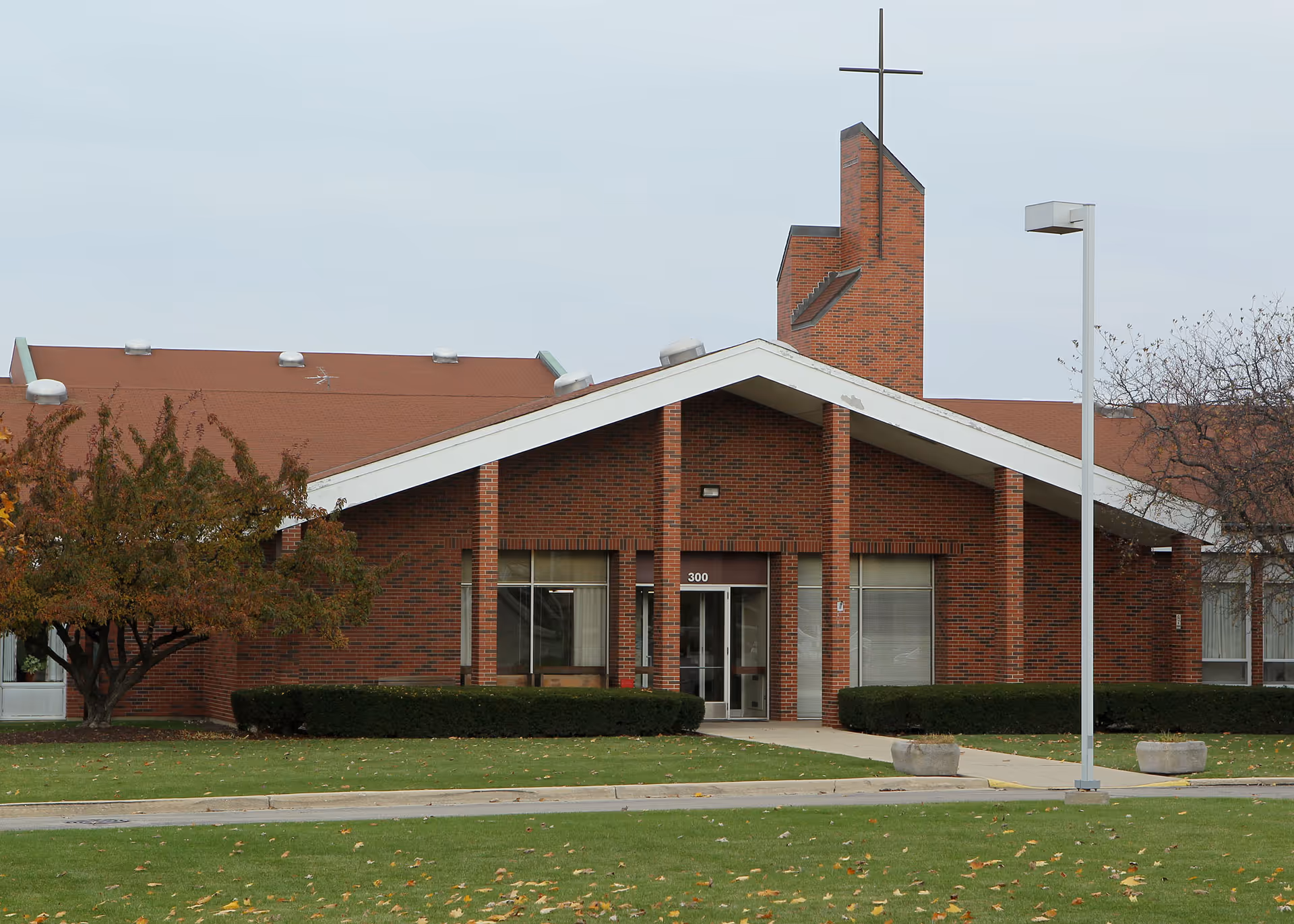 Brick senior living facility with peaked entrance, glass doors, and cross atop the roof.