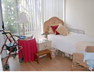 A bright bedroom with a single bed, walker, nightstand, and wicker chair.