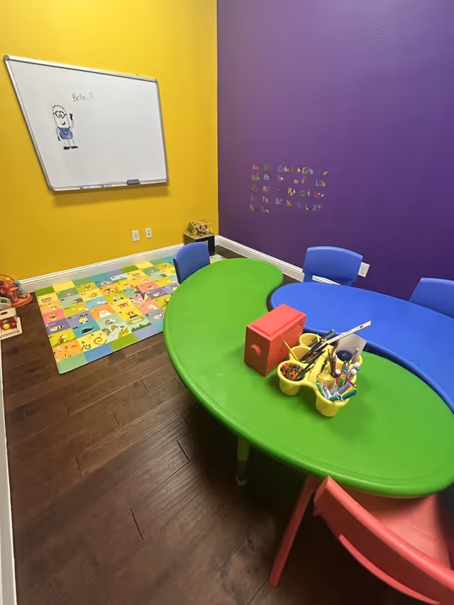 Colorful playroom inside a senior facility with curved green table, blue chairs, and toys.
