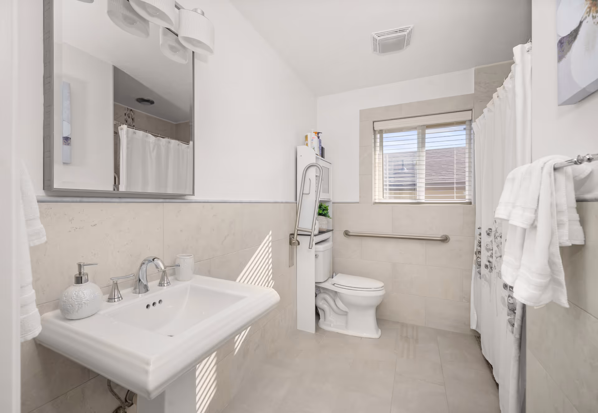 Bright accessible bathroom featuring sink, toilet, shower curtain, and window.
