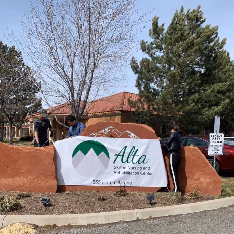 Outdoor scene with Alta Skilled Nursing and Rehabilitation Center sign on a rock barrier.