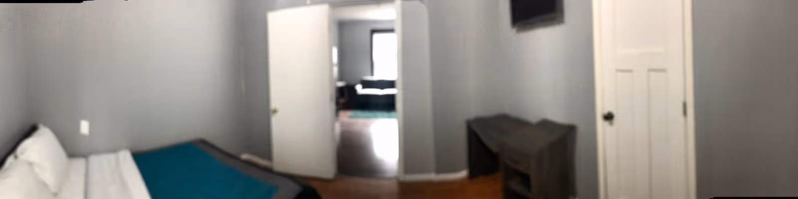Narrow bedroom in a senior living facility with a bed along the left wall and doorway.