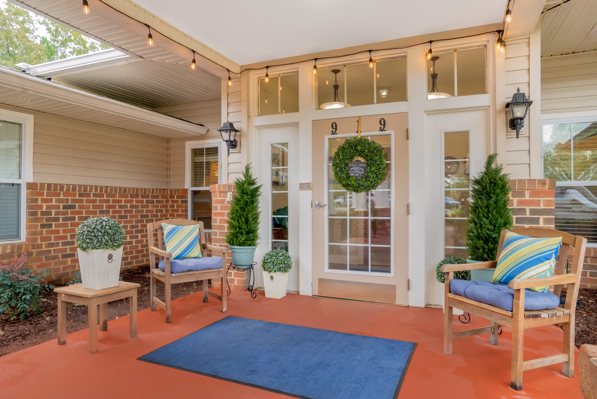 Front porch of Brookdale Monroe Square featuring chairs, wreath, string lights, and potted plants.