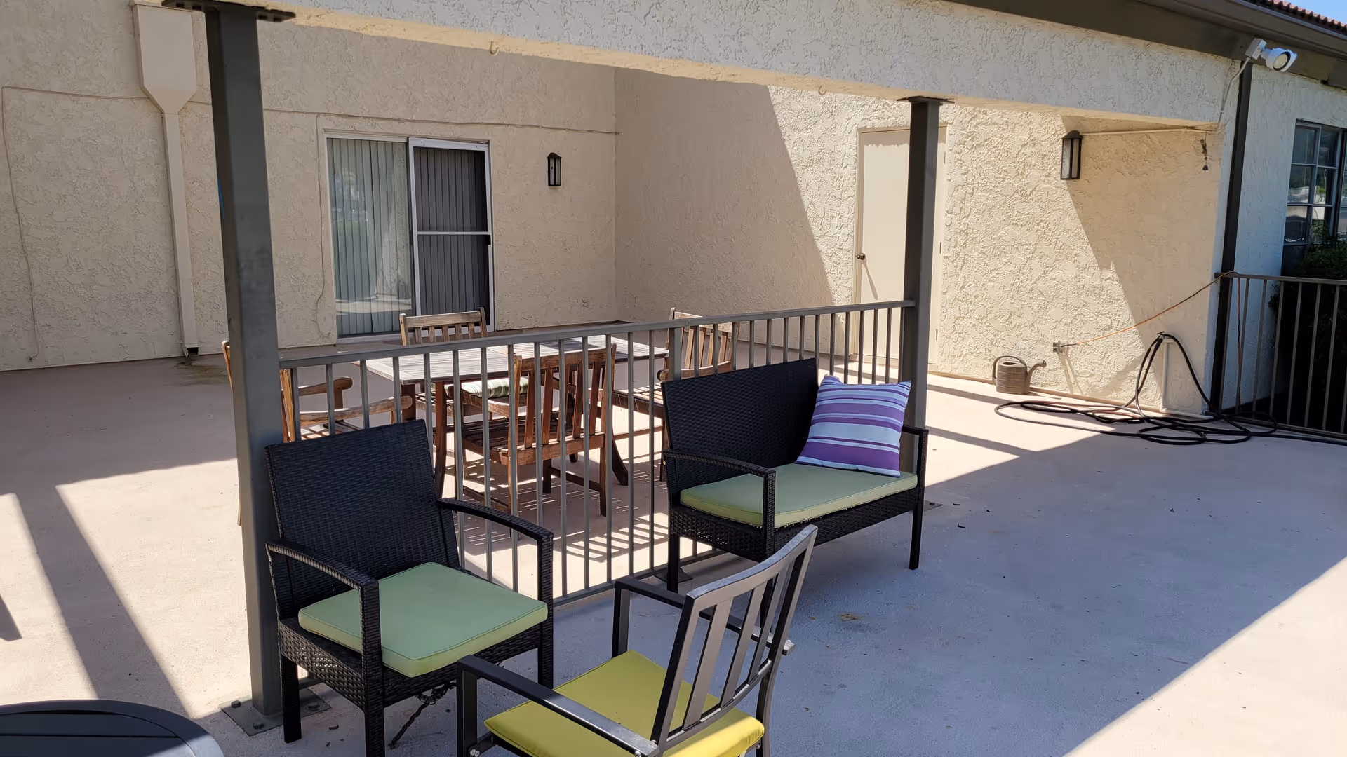 Outdoor patio with wicker chairs and a table on a concrete balcony beside a beige building.