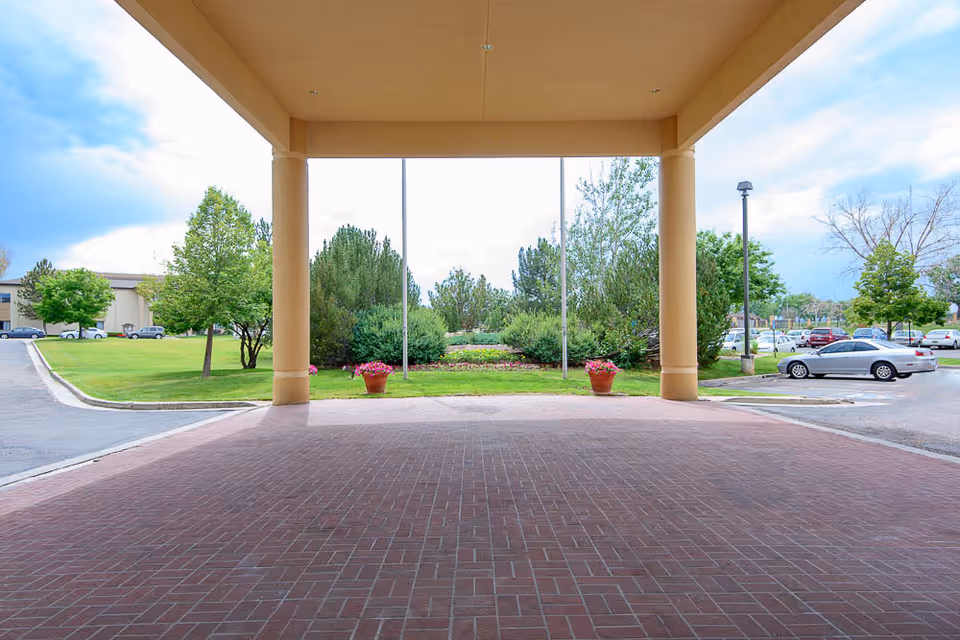 Covered entrance with columns and a brick-paved driveway at a senior living facility.