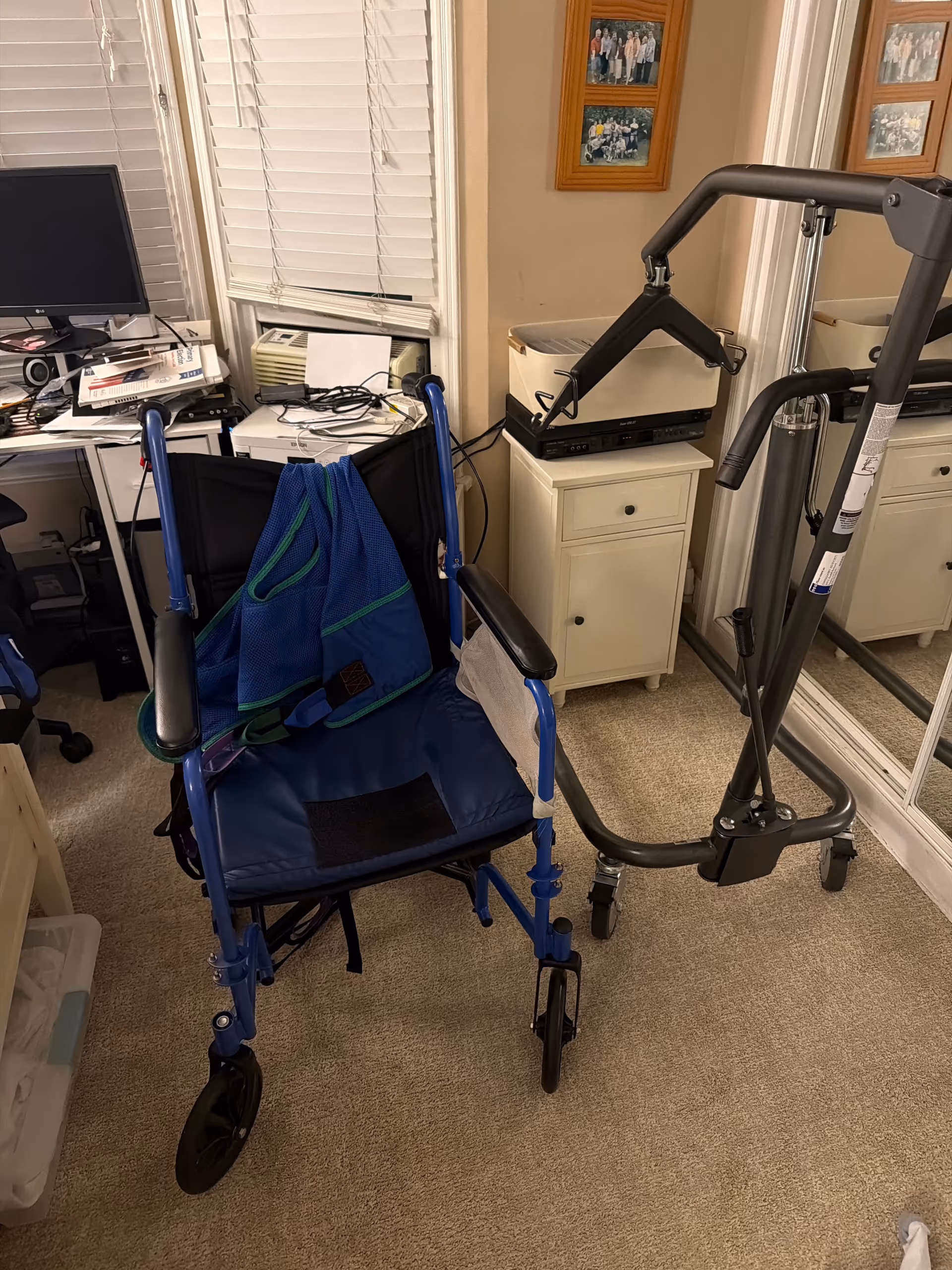 Indoor home care room with wheelchair, walker, desk, printer, and blinds.