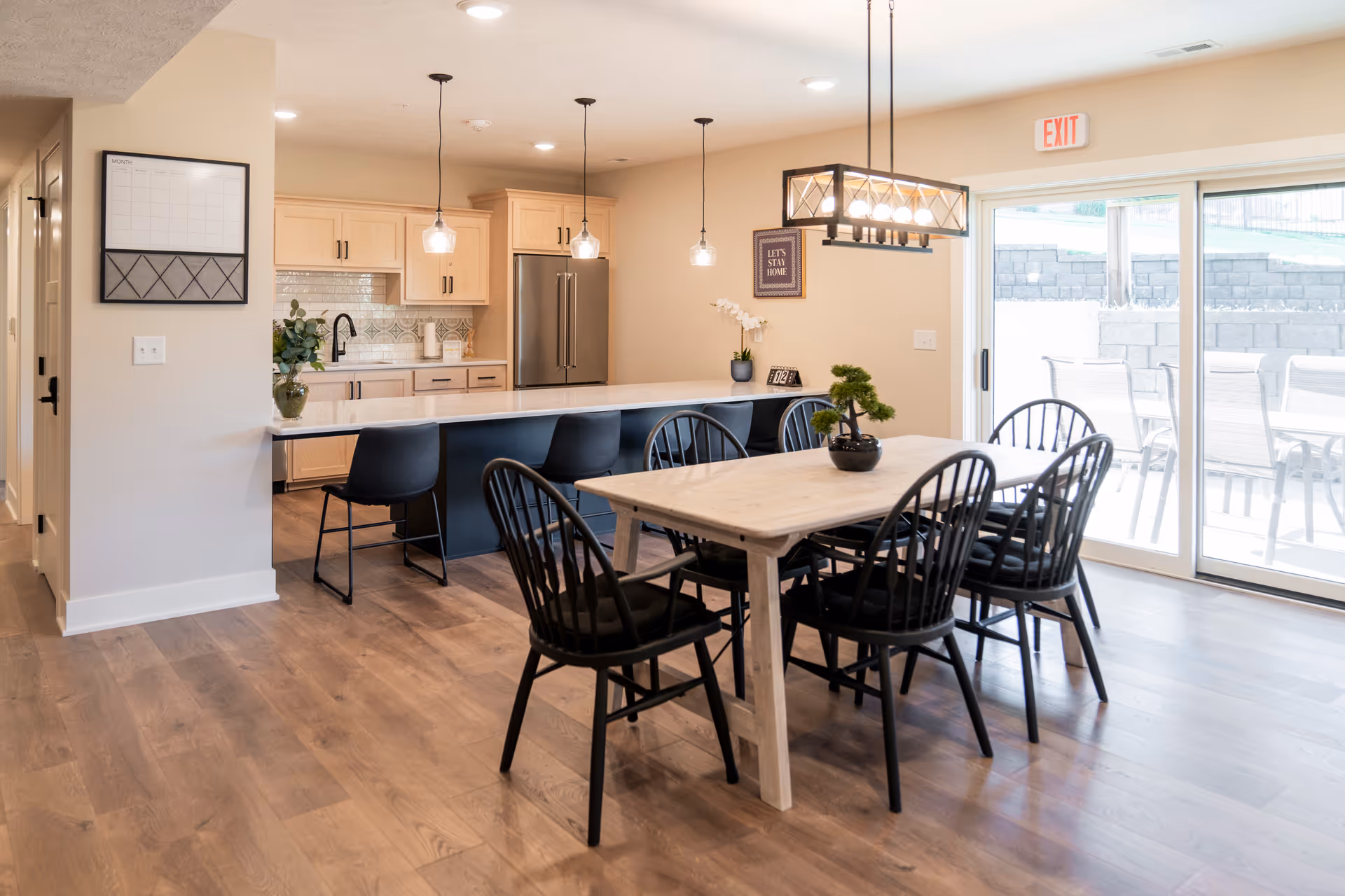 Bright open kitchen and dining area with a wooden table, pendant lights, and black chairs.