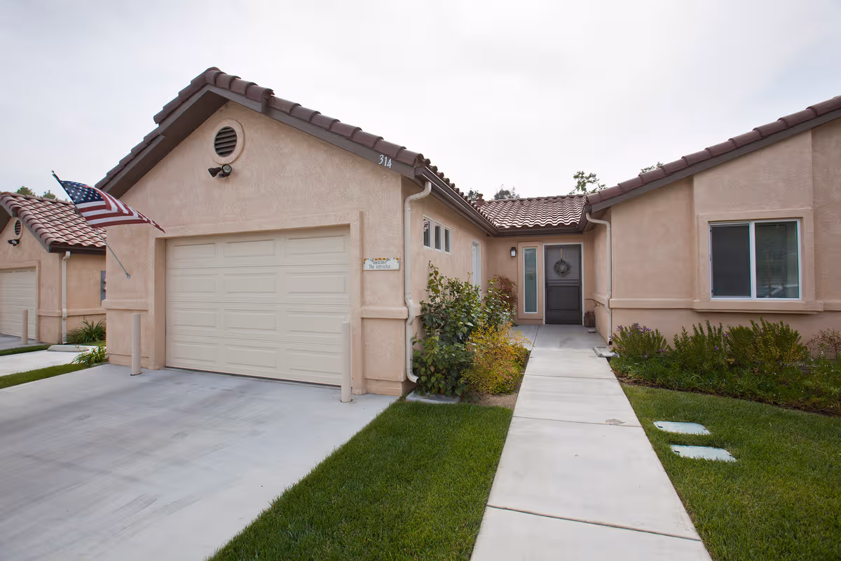 Beige stucco senior living townhomes with a two-car garage, walkway, and manicured lawn.