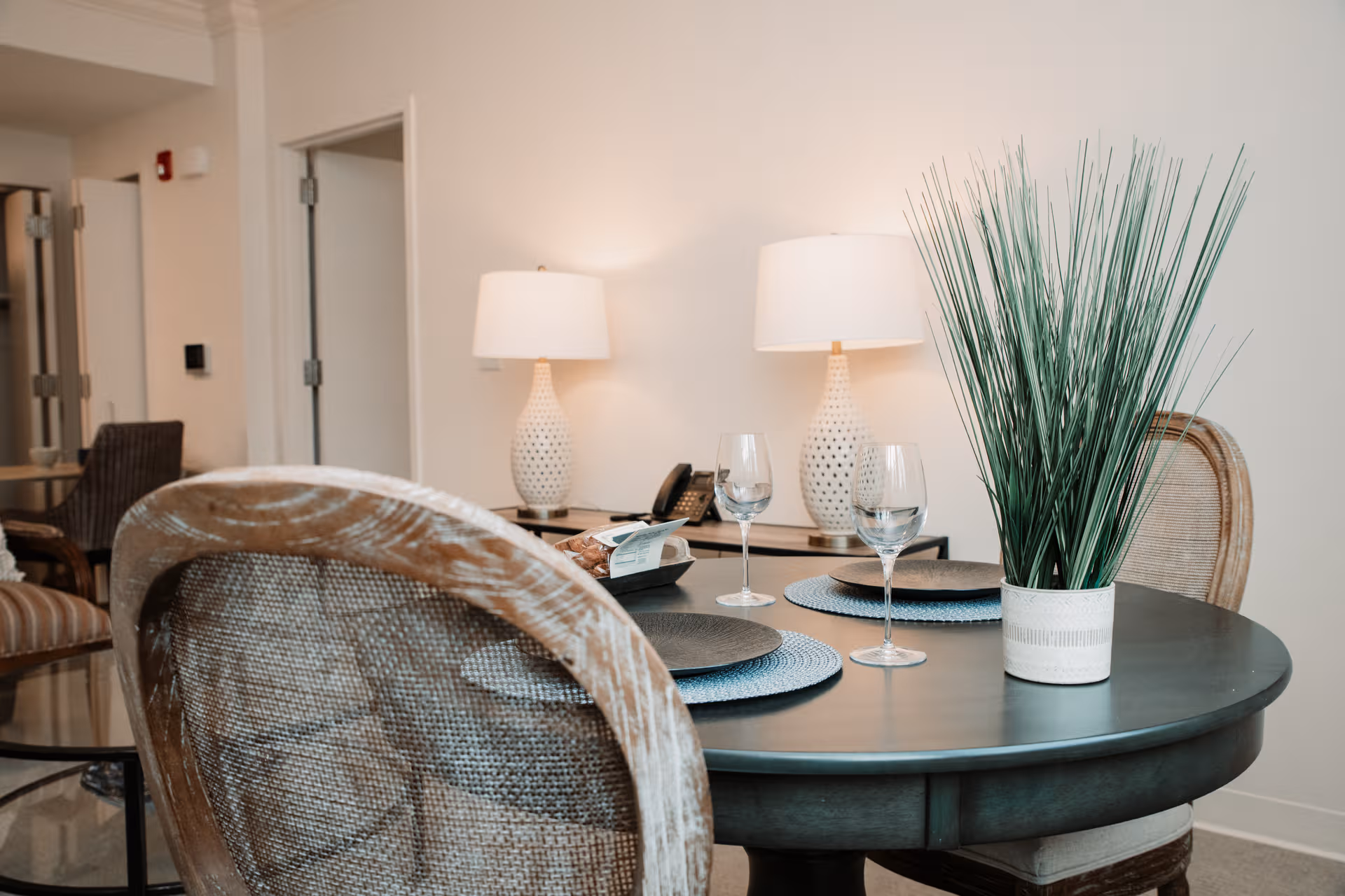 Round dining table set with plates, wine glasses, a tall plant centerpiece, and soft lighting.